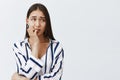 Horizontal shot of anxious good-looking female student in striped blouse, biting fingernail nervously, frowning and