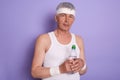 Horizontal shot of attentive serious man holding bottle of water, wearing sports suit, doing physical exercises, looking directly Royalty Free Stock Photo