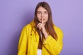 Horizontal shot of attractive woman with long beautiful hair, keeping finger near lips, calls on to keep silence, covering her Royalty Free Stock Photo