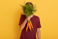 Horizontal shot of attracvtive man holding bunch of fresh carrots, young model isolated over yellow background, handsome guy Royalty Free Stock Photo