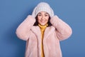 Horizontal shot of beautiful cheerful female wearing faux fur coat, sweater, gloves and hat, looking directly at camera, putting Royalty Free Stock Photo