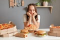 Horizontal shot of bored sad upset woman with brown hair wearing white T-shirt sitting at table, keeping diet, looking at fast