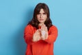 Horizontal shot of brunette female holding in hand plastic menstrual cup and showing stop gesture with palm posing isolated over