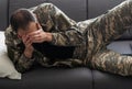Horizontal shot of Caucasian military man wearing camouflage uniform sitting on sofa, soldier holding cell phone
