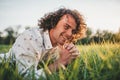 Horizontal shot of cheerful handsome young male model with curly hair, smiling, relaxing atcomfortable green lawn in the park. Royalty Free Stock Photo