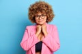 Horizontal shot of cute pretty busty woman with curly hair in transparent spectacles keeps clenched fists under chin Royalty Free Stock Photo