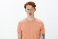 Horizontal shot of displeased moody and picky cute redhead male with tattoos and freckles in glasses, wrinkling nose and