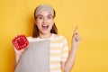 Horizontal shot of excited Caucasian woman looking at camera prepares for sleep holds soft pillow dressed in sleepmask on forehead