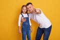 Horizontal shot of fashionable young father pointing finger at camera, showing something to his daughter, dad and female kid Royalty Free Stock Photo