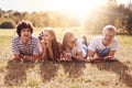 Horizontal shot of four happy friends lie on ground, have picnic during sunny summer day, have positive expressions, smile pleasan