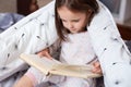 Horizontal shot of girl reading under blanket with dandelion, having serious facial expression, looks concentrated, charming Royalty Free Stock Photo