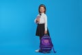 Horizontal shot of girl wearing backpack and school uniform, holding books Royalty Free Stock Photo