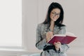 Horizontal shot of good looking woman professor writes down text notes in notepad, prepares for lecture in university, wears Royalty Free Stock Photo