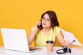 Horizontal shot of gorgeous young woman having cell phone conversation while sitting front open laptop computer, female person Royalty Free Stock Photo