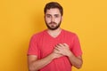 Horizontal shot of handsome man wering casual outfit isolated over yellow background, keeping hands on chest, expressing gratitude