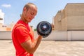 Horizontal shot of handsome muscular man lifts dumbbell outdoor, gets ready for weight lifting training, has muscular Royalty Free Stock Photo