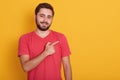 Horizontal shot of handsome unshaven male, dressed in casual red t shirt, looking directly at camera, pointing with index finger