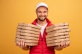 Horizontal shot of happy man holds two piles of carton boxes with pizza, has surprised joyful expression, works as courier in