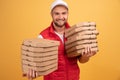 Horizontal shot of happy man holds two piles of carton boxes with pizza, has surprised joyful expression, works as courier in