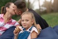 Horizontal shot of happy mother and father kissing while sitting on frameless chair in park with little daughter, cute blonde kid Royalty Free Stock Photo