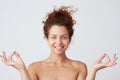 Horizontal shot of happy peaceful yong woman with perfect skin after applying cream or mask shows meditation gesture by hands