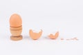 Horizontal shot hen egg in old wooden egg stand and multiple broken egg shells on a white surface. Minimalism. Conceptual art for