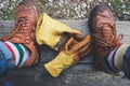 Horizontal shot of human feet with brown shoes and a pair of yellow gloves on a wooden bench