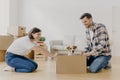Horizontal shot of lovely woman moves cardboard box with small puppy to husband side, spend free time together, move in new modern