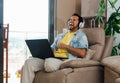 Horizontal shot of a male listening to music, working with laptop and laughing with closed eyes Royalty Free Stock Photo