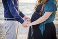 Horizontal shot of a man in blue shirt and a pregnant woman in black dress holding hands on beach Royalty Free Stock Photo