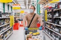 Horizontal shot of man walks in supermarket with shopping trolley with goods, wears medical mask and rubber gloves, food running Royalty Free Stock Photo