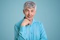 Horizontal shot of mature grey haired Caucasian male pensioner wears elegant shirt, keeps hand under chin, poses for making photo