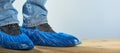 Man with blue shoe covers worn over classic shoes on gray background, closeup. Photo with copy space