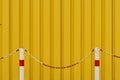 Horizontal shot of a metallic yellow wall with two white, red-striped poles with chains in front Royalty Free Stock Photo