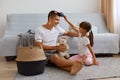 Horizontal shot of optimistic dark haired male with his female child playing together at home, sitting on floor near cough in