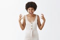 Horizontal shot of outraged scary woman in white overalls with afro hairstyle gesturing hands with angry and pissed