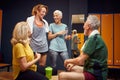 Horizontal shot of people in locker room, senior man and two women with young trainer having a joyful conversation before workout