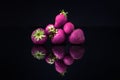 Horizontal shot of a pile of purple strawberries with a reflection on a black surface