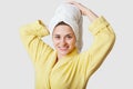 Horizontal shot of pleasant looking cheerful young female model keeps hands on towel at head, dressed in domestic clothes, feels