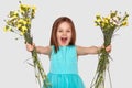 Horizontal shot of pleased small child holds two bouquets of flowers, opens mouth opened, exclaims with happiness, wears blue Royalty Free Stock Photo