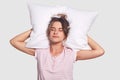 Horizontal shot of restful lovely young female with closed eyes, keeps pillow behind head, sees pleasant dreams during night time, Royalty Free Stock Photo