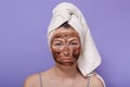 Horizontal shot of serious attractive young female looking directly at camera, having applied coffee scrub on face, cleaning skin