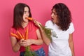 Horizontal shot of shocked emotional female having carrot in mouth, eating vegetables. Charismatic brunette giving vegetables for