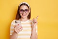 Horizontal shot of smiling happy young woman wearing striped t-shirt posing isolated over yellow background, holding cell phone Royalty Free Stock Photo