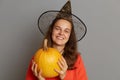 Horizontal shot of smiling optimistic attractive woman holding big ripe orange pumpkin, looking at camera with toothy smile,