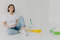 Horizontal shot of smiling woman designer chooses best color for apartment, holds palette, dressed in casual clothes, paints walls Royalty Free Stock Photo