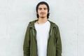 Horizontal shot of stylish teenage boy wears black hat, white t shirt and green anorak, looks with satisfied expression direclty a