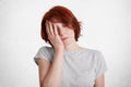 Horizontal shot of tired bored female with short hairstyle, closes eyes and covers face with hand, being overworked, isolated over