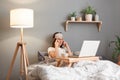 Horizontal shot of tired sick unhealthy woman wearing sleeping mask posing in front of laptop at home while lying on bed, Royalty Free Stock Photo