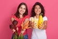 Horizontal shot of two brunette caucasian women holding vegetables in hands, females gardeners showing their harvest: zucchini, Royalty Free Stock Photo
